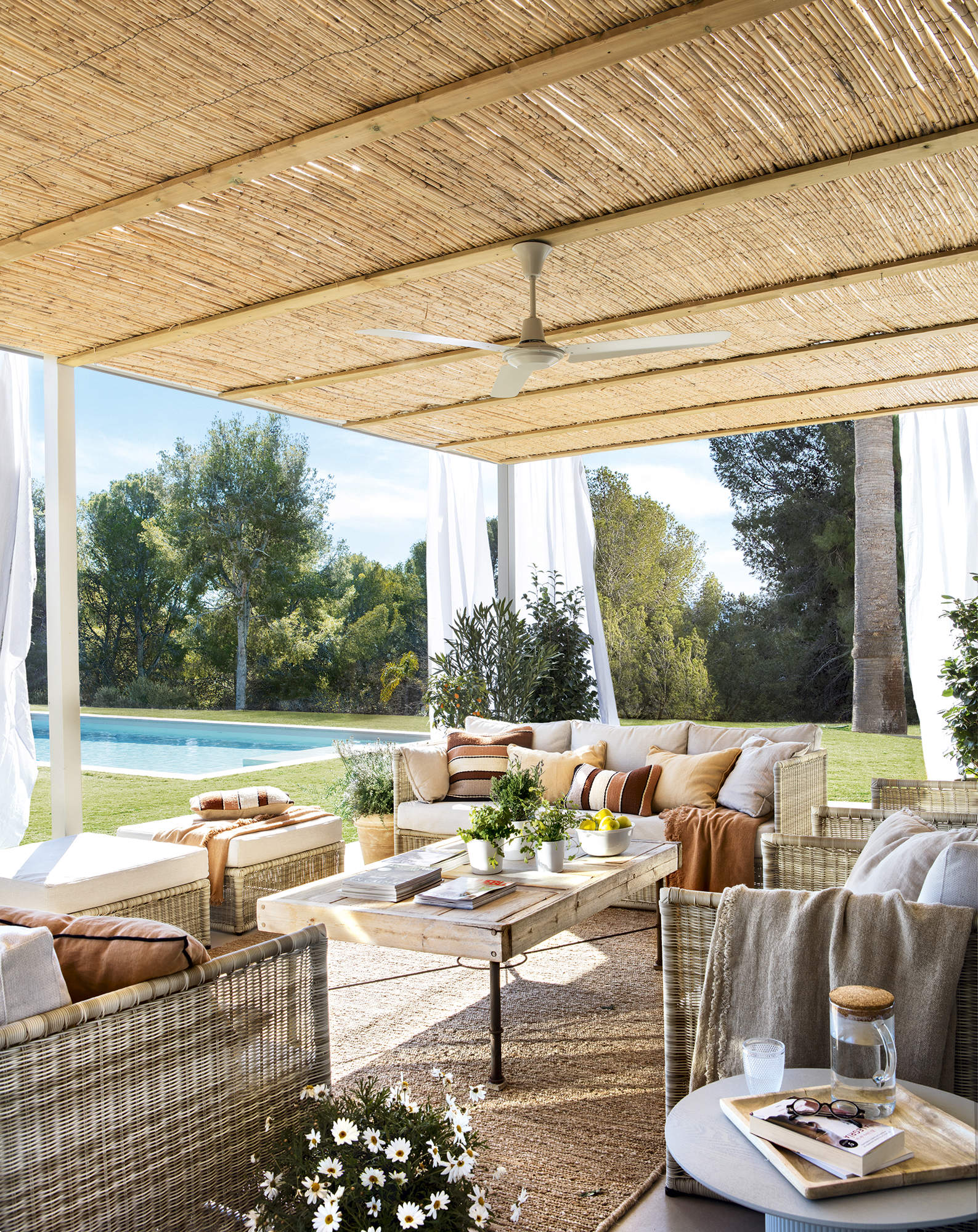 Porche con salón en un jardín con piscina.